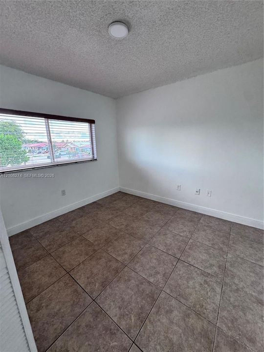 Interior space featuring white walls,ceramic tile flooring, a dual-pane horizontal sliding window with attached blinds, and a circular flush-mount ceiling light fixture