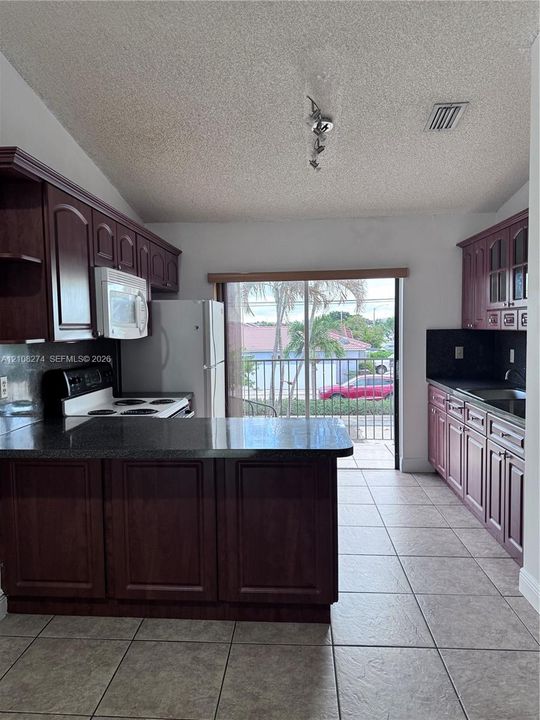 Kitchen featuring dark-toned cabinetry, dark countertops, a peninsula, tile flooring, and a sliding glass door