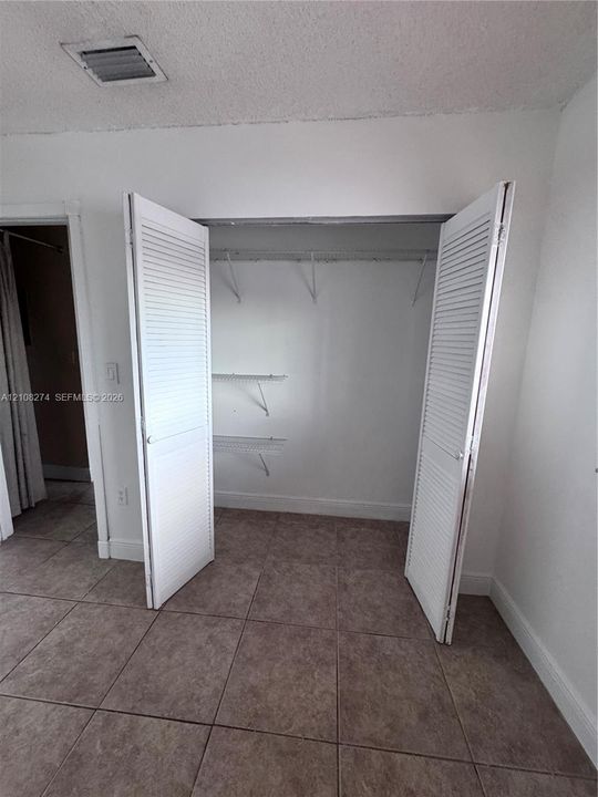 Closet featuring white louvered bifold doors and built-in wire shelving units, complemented by neutral tile flooring