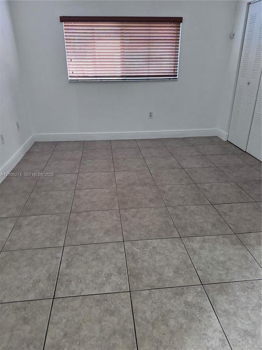 Interior space featuring neutral tile flooring, white walls, louvered closet doors, window with horizontal blinds