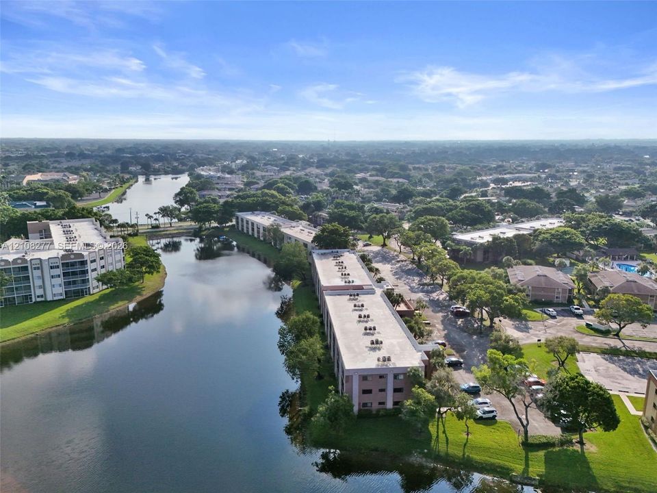 Aerial perspective of waterfront multi-story buildings featuring paved parking, manicured landscaping, and mature trees