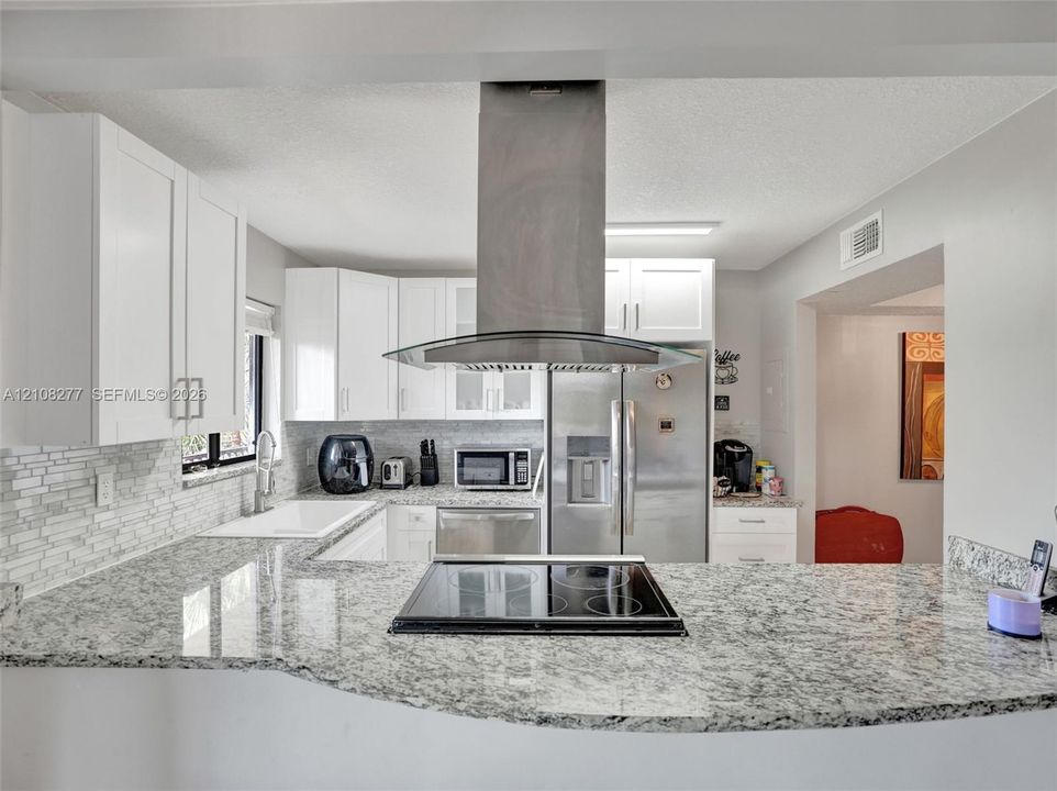 Kitchen featuring stone-finish countertops, stainless steel chimney-style range hood, electric cooktop, white cabinetry, and a subway tile backsplash