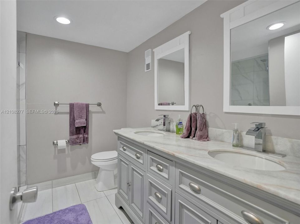 Double vanity featuring stone-finish countertops, undermount sinks, polished chrome faucets, and shaker-style cabinetry with dual wall-mounted mirrors