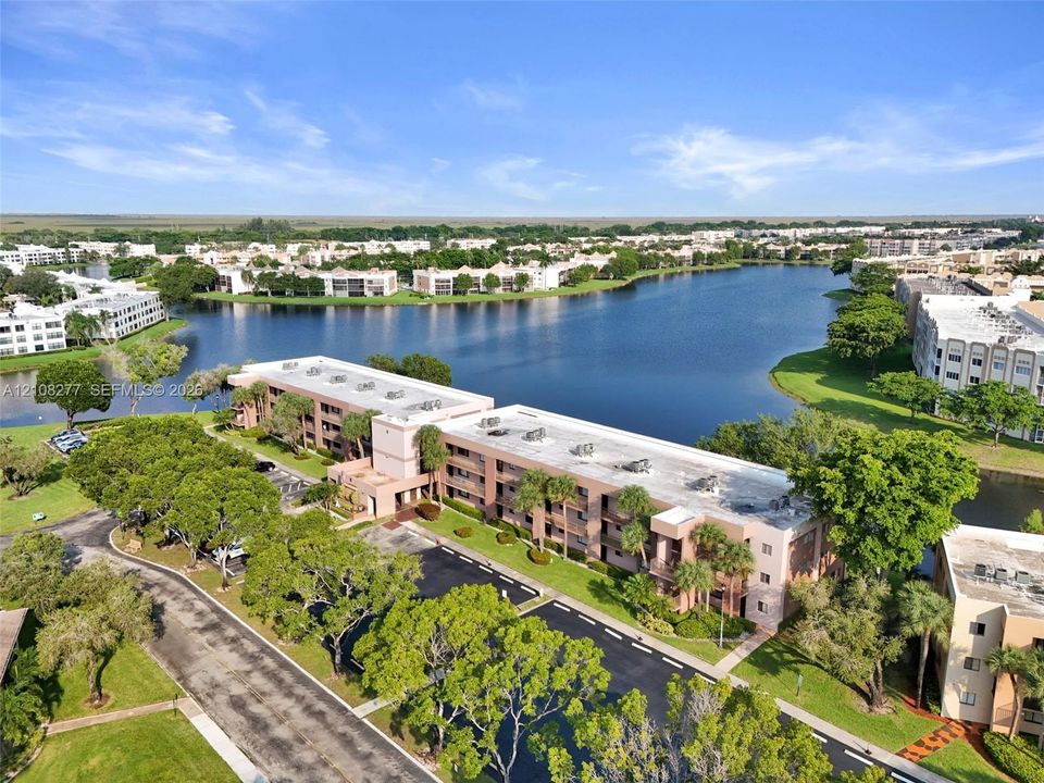 Aerial perspective of a multi-story residential building featuring a flat roofline, paved parking area, mature landscaping, and an expansive waterfront setting