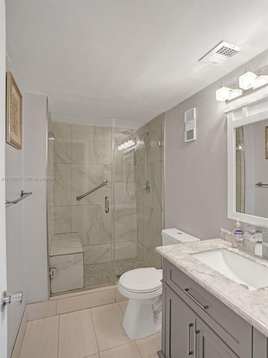 Bathroom featuring a dark-finish vanity with a stone-top integrated sink, glass-enclosed shower with tile surround and built-in bench, and polished chrome fixtures