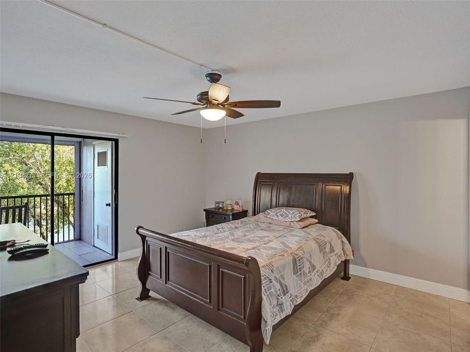 Large-format tile flooring, ceiling fan with integrated lighting, and a sliding glass door providing access to a private balcony