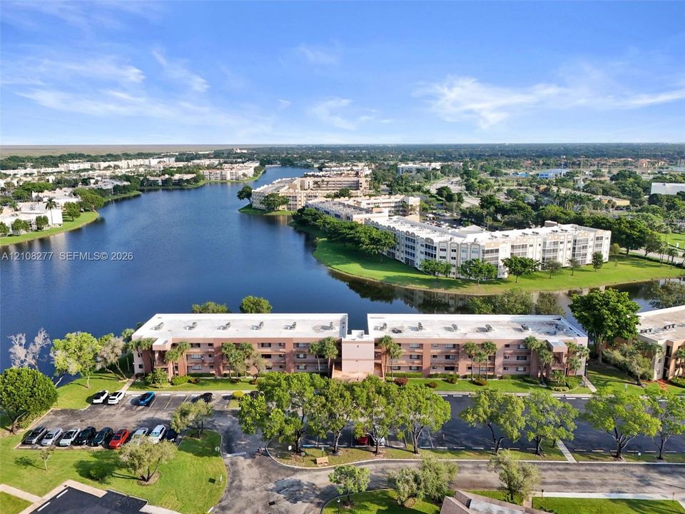 Aerial perspective of a multi-story residential building featuring exterior masonry cladding, paved parking areas, and mature landscaping situated on a waterfront lot