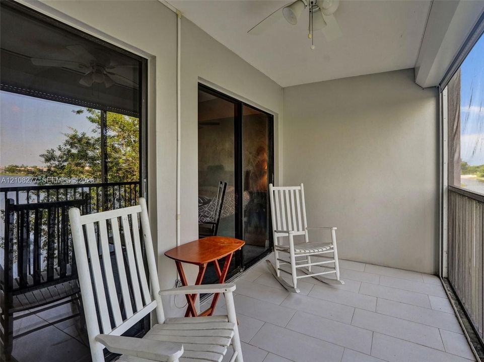 Covered balcony featuring neutral tile flooring, dual sliding glass door access, a mounted ceiling fan, and screened enclosures