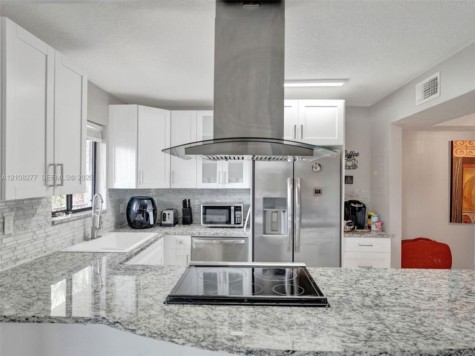 Kitchen featuring stone-finish countertops, stainless steel appliances, a glass and stainless steel island-mounted range hood, shaker-style cabinetry, and a stacked-tile backsplash