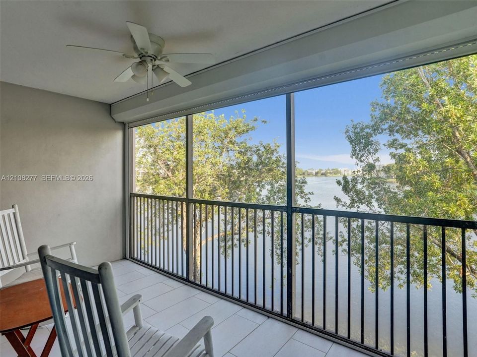 Screened balcony featuring tile flooring, a ceiling fan, and metal railings overlooking a lake and surrounding trees