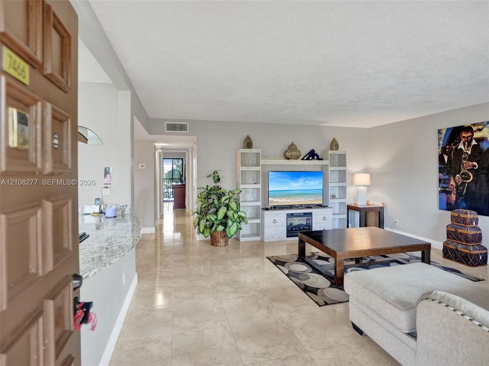 Open-concept interior featuring neutral stone-finish tile flooring, a stone-surfaced breakfast bar, and a built-in media center with integrated fireplace