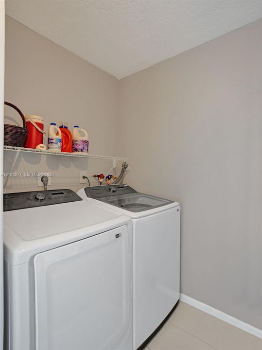 Dedicated laundry space featuring neutral wall paint, tile flooring, and wall-mounted wire shelving