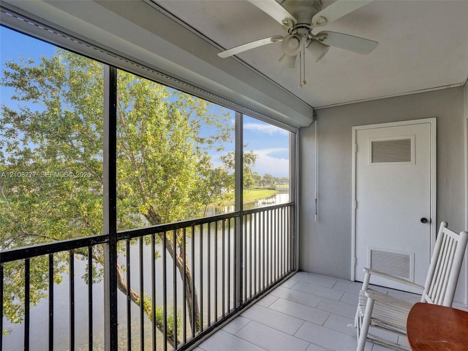 Screened-in balcony featuring tile flooring, a ceiling fan, and metal railings overlooking a water feature