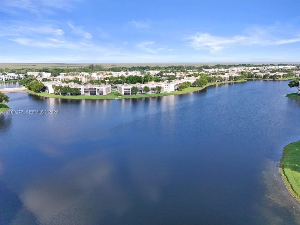Aerial perspective of multi-unit residential structures situated along a large body of water, featuring expansive water frontage and mature landscaping