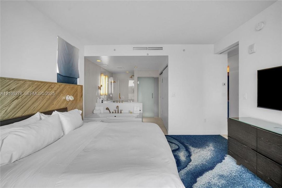 Custom wood-slat headboard feature wall, integrated soaking tub, recessed lighting, and wall-mounted plumbing fixtures