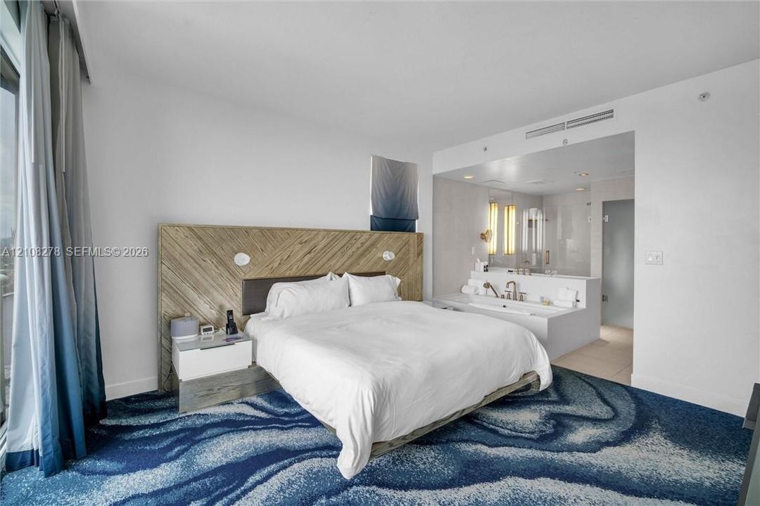 Wood-finish slat accent wall, built-in bedside cabinetry, recessed ceiling lighting, and a soaking tub with integrated vanity