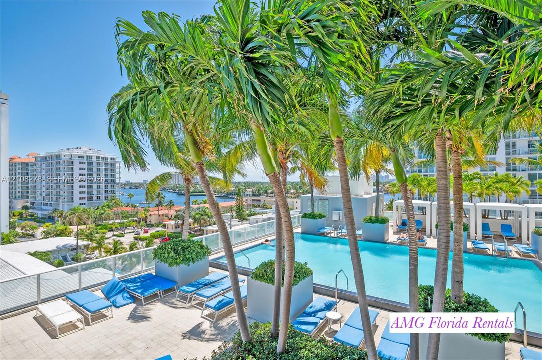 Elevated swimming pool featuring a tile deck, glass panel perimeter railing, built-in planters, and palm tree landscaping