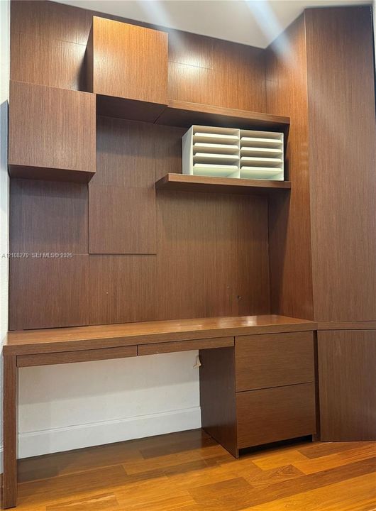 Custom built-in wood cabinetry featuring a desktop surface, integrated storage drawers, shelving, and wood-finish flooring