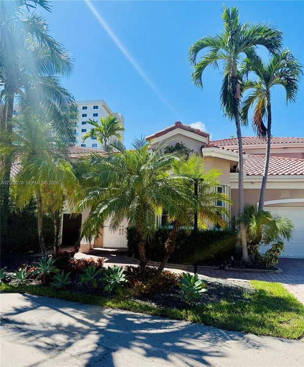 Stucco exterior featuring a terracotta tile roof, paver driveway, attached garage, and mature palm landscaping