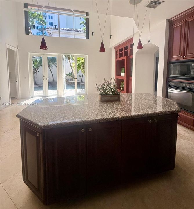 Kitchen island with a stone countertop and dark wood-finish cabinetry, vaulted ceilings, multi-light pendant fixture, double wall oven, and French doors featuring transom windows