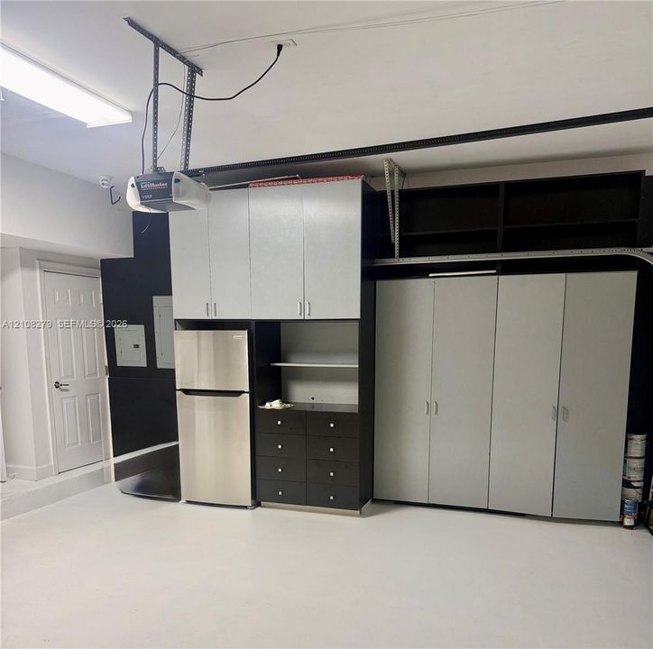 Garage featuring extensive built-in cabinetry, integrated shelving, an inset stainless steel refrigerator, and overhead fluorescent lighting