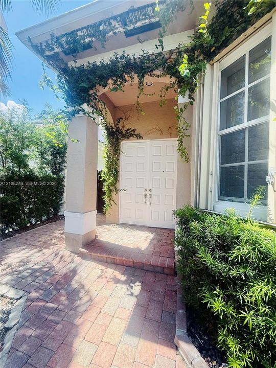 Covered entryway featuring a brick paver walkway, double doors with paneled detailing, a neutral-toned exterior, and integrated structural columns
