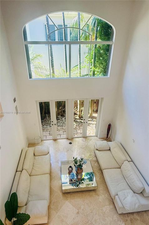 Double-height room featuring vaulted ceilings, a large arched window, and dual glass-paned doors with stone tile flooring