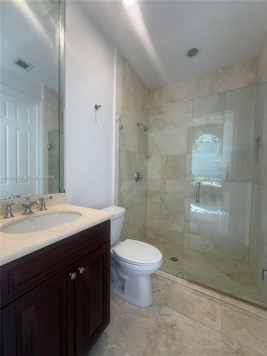 Dark wood-finish vanity with a light-toned countertop, undermount sink, and polished metal hardware, paired with a glass-enclosed shower featuring tile walls and matching tile flooring