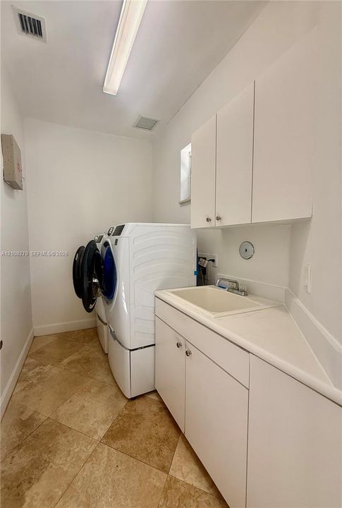 Utility room featuring tile flooring, white shaker-style cabinetry, a drop-in basin sink, and overhead fluorescent lighting