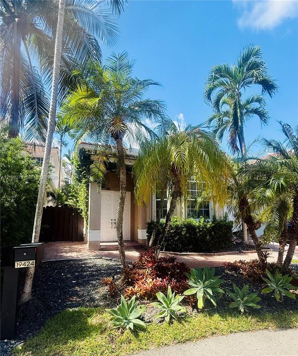 Exterior featuring double-door entry, brick-paved walkway, mature palm trees, and established ornamental landscaping