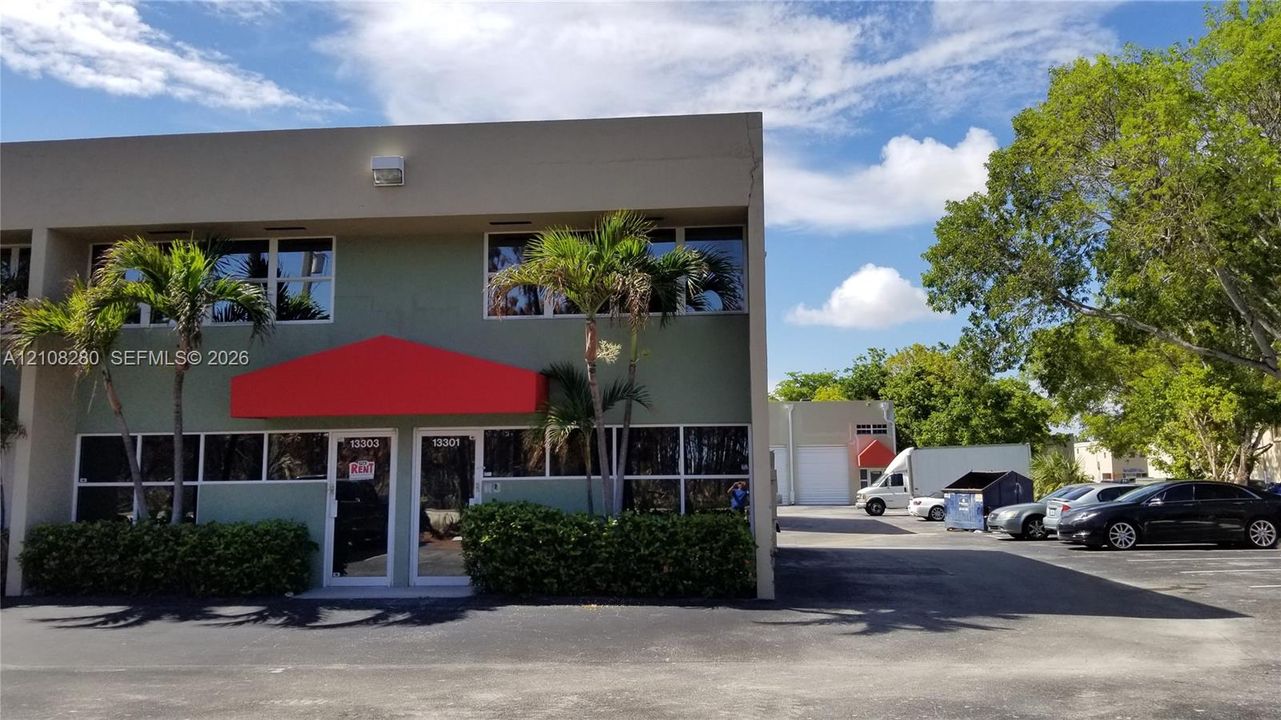 Two-story commercial building featuring a stucco exterior, expansive glass-paneled ground floor windows, integrated exterior lighting, and a paved parking lot