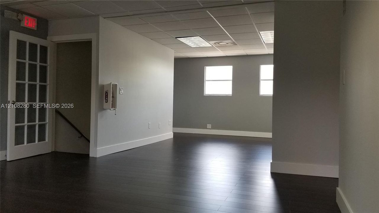 Interior space featuring wood-finish flooring, a glass-paneled door, recessed ceiling grid lighting, and neutral-toned wall paint