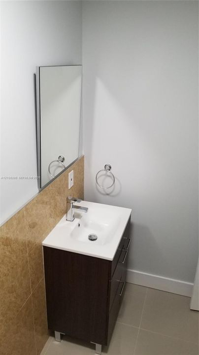 Modern vanity featuring a white rectangular sink, metallic hardware, and storage drawers, complemented by a stone-finish backsplash, wall-mounted mirror, and circular towel ring