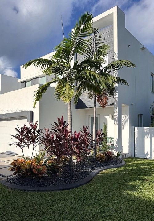 Modern contemporary exterior featuring clean white stucco siding, a recessed entryway, an integrated garage, and curated landscaping with mature palm trees and dark stone mulch
