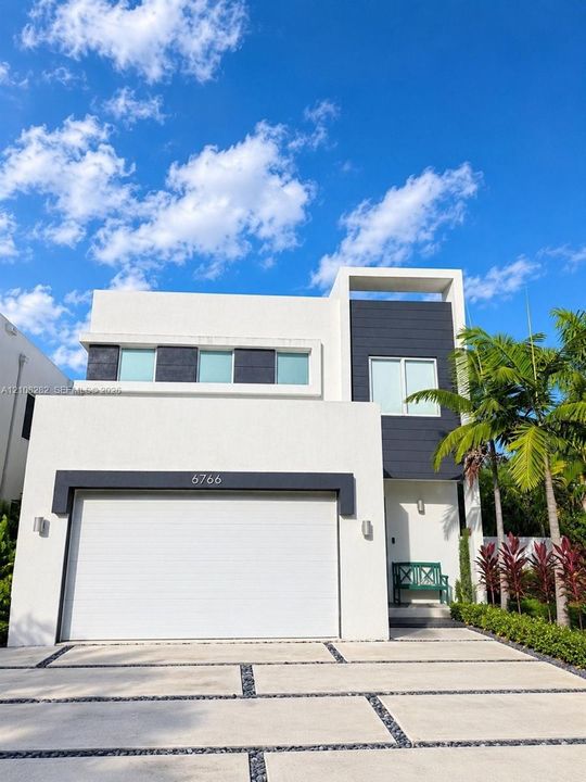 Contemporary two-story exterior featuring a white stucco facade with dark contrasting panels, horizontal sliding windows, and a segmented concrete driveway with dark stone inlays