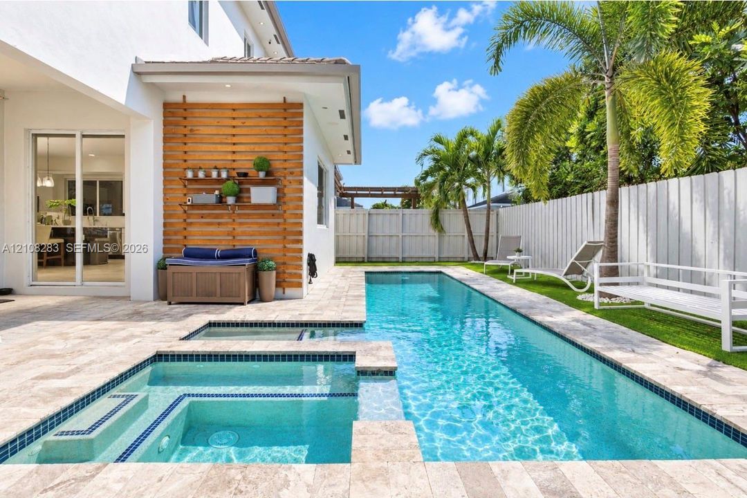 Custom pool with integrated spa featuring stone-tiled decking, decorative wood-slat accent wall, and perimeter fencing