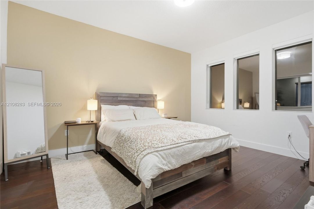 Room featuring wood-finish flooring, three vertical windows, and a neutral-toned accent wall