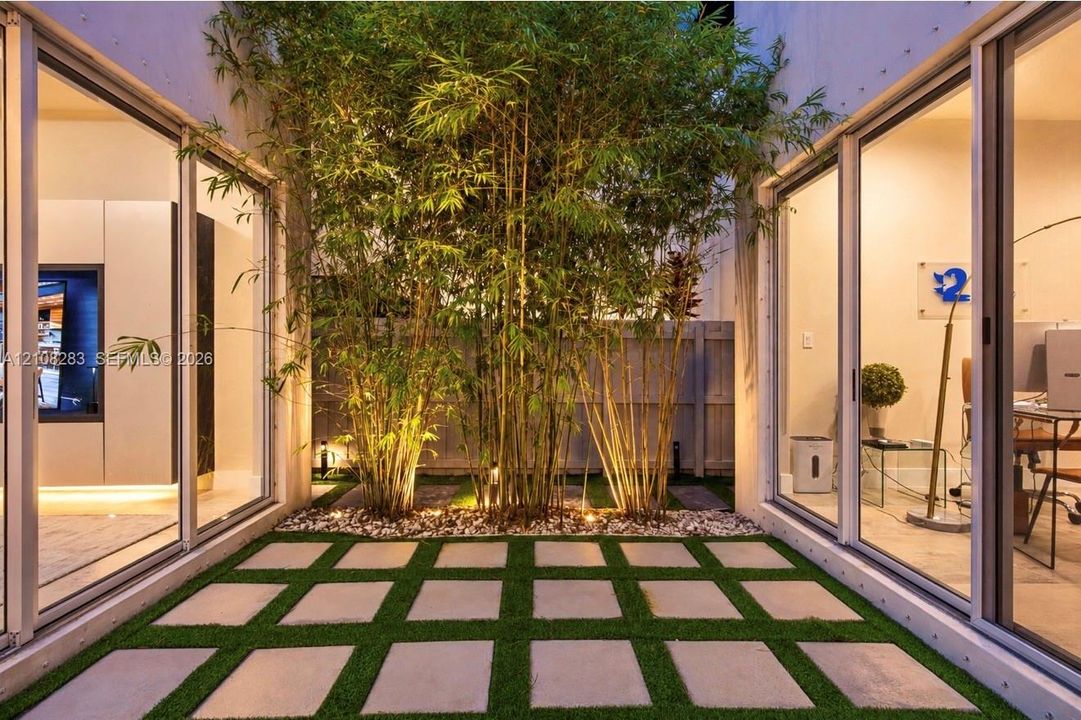 Central atrium featuring large-format concrete pavers, integrated synthetic turf grid, mature bamboo specimens, and expansive floor-to-ceiling sliding glass doors