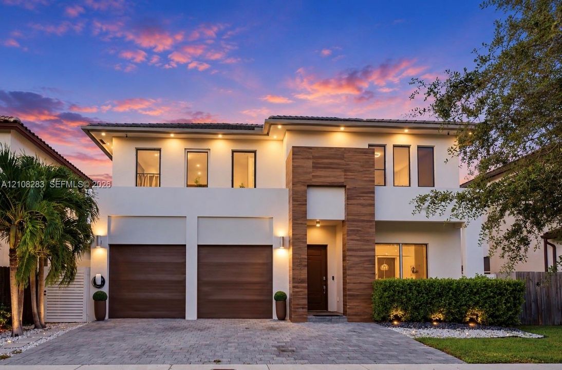 Two-story contemporary exterior featuring stucco siding, vertical wood-finish accents, dual-car garage, recessed exterior lighting, and a paved stone driveway