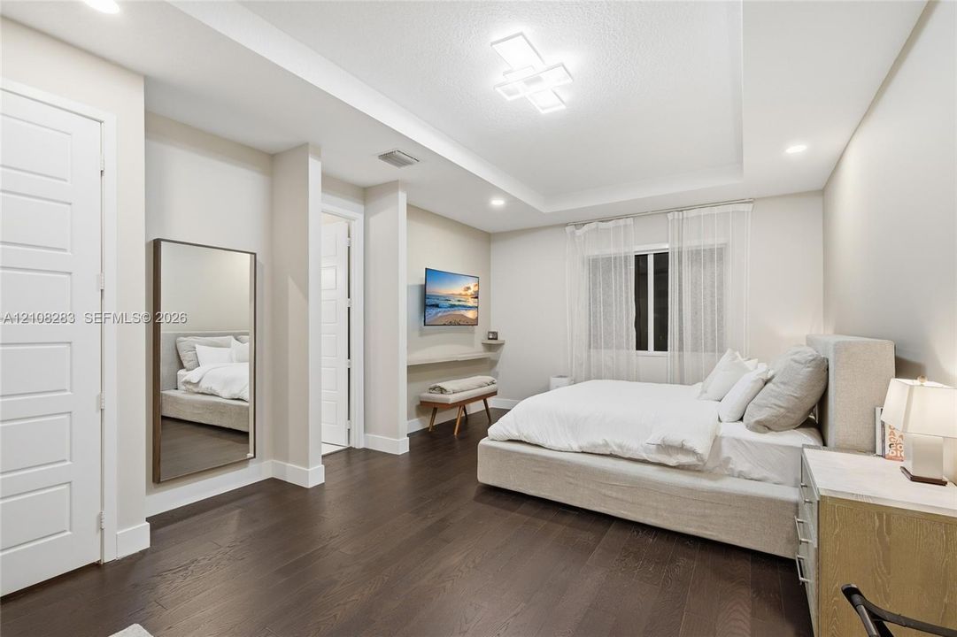 Bedroom featuring wood-finish flooring, tray ceiling with recessed and geometric modern lighting, and a wall-mounted floating display ledge