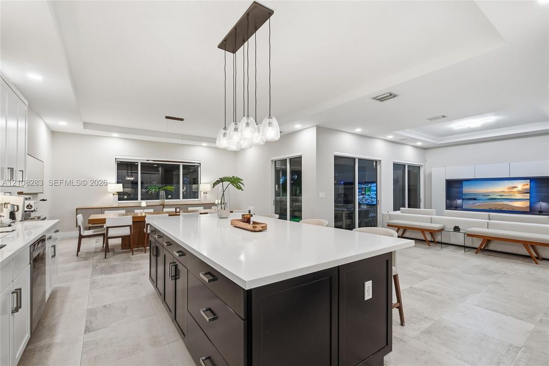 Kitchen featuring a center island with contrasting cabinetry, stone-finish countertops, tile flooring, built-in media console, and multi-pendant lighting