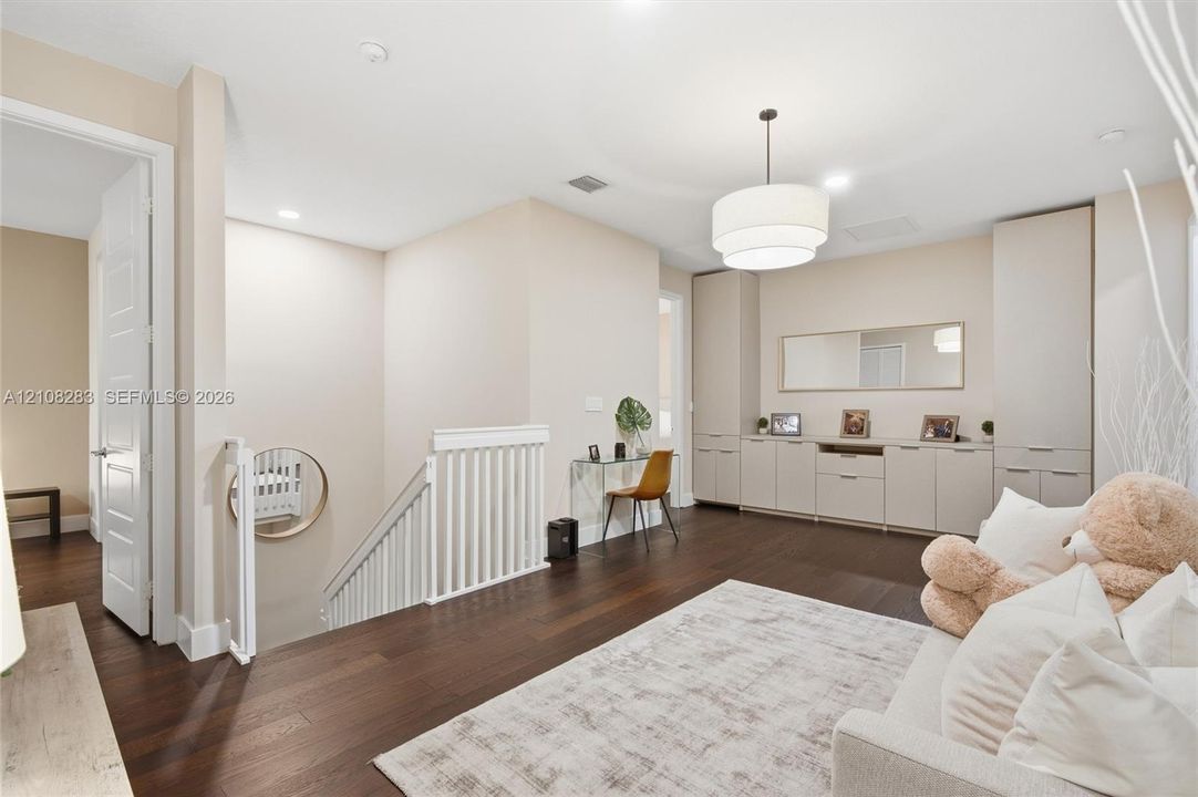 Dark wood-finish flooring, built-in floor-to-ceiling cabinetry with integrated storage, white spindle staircase railing, and a tiered drum pendant light fixture