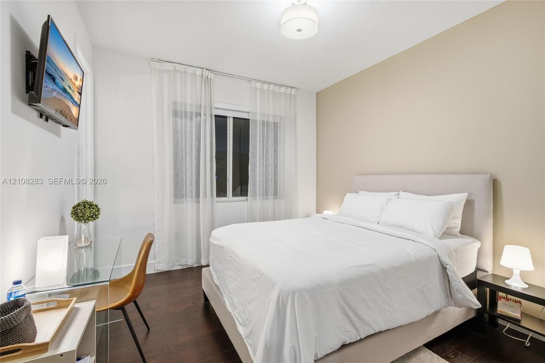 Room featuring dark wood-finish flooring, neutral-toned accent wall, and a central ceiling-mounted drum light fixture