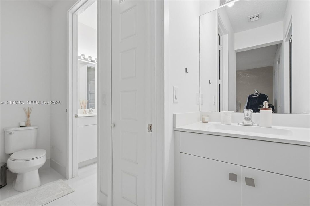 Bathroom featuring a white vanity cabinet with a stone-top integrated sink, a full-height wall mirror, a polished chrome faucet, and a standard-height toilet