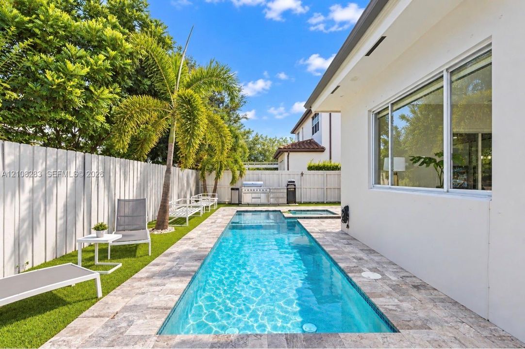 Private backyard featuring an inground lap pool, integrated spa, stone-finish decking, artificial turf, and a perimeter privacy fence