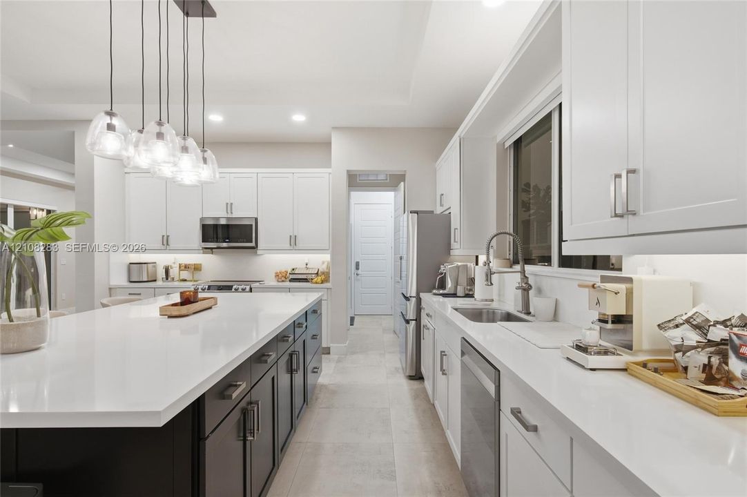 Kitchen featuring a central island with a solid-surface countertop, white shaker-style cabinetry, stainless steel appliances, and multi-light pendant fixture