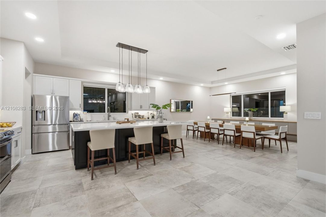 Kitchen featuring a center island with contrasting cabinetry, stone-finish countertops, stainless steel appliances, recessed ceiling lighting, and large-format tile flooring