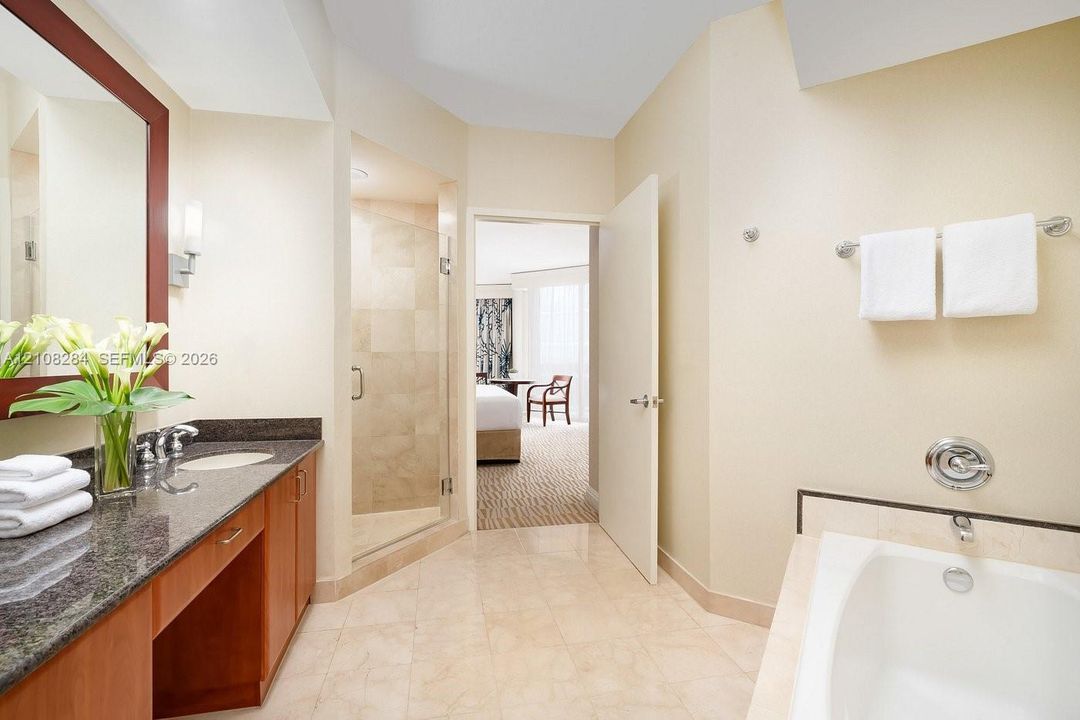 Bathroom featuring a stone-surface vanity with undermount sink, walk-in tile shower with glass enclosure, deep soaking tub, and tile flooring