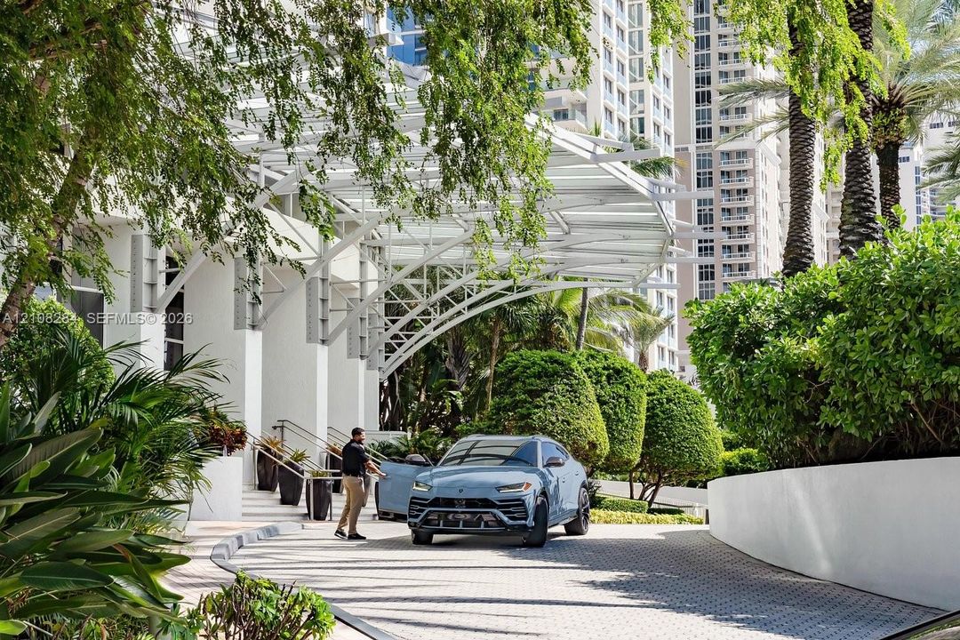 Porte-cochere entrance featuring white structural steel framing, paved circular driveway, and mature perimeter landscaping