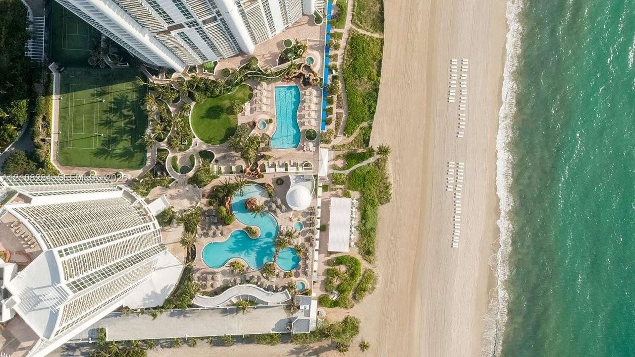 Aerial perspective featuring direct beach access, multiple outdoor swimming pools, a tennis court, and manicured grounds